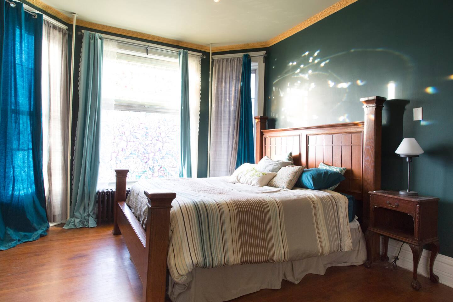 Teal bedroom with king bed, blue curtains and hardwood floor